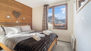 Une chambre à coucher avec une tête de lit en bois, un lit recouvert de draps blancs, une couverture sombre et une fenêtre donnant sur les montagnes.