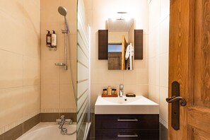 Un bany modern amb un box de dutxa de vidre, un lavabo blanc i mobles de tocador foscos, i una porta de fusta.