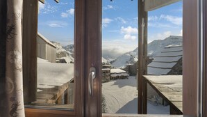 Une vue à travers une fenêtre à cadre en bois, donnant sur un paysage enneigé, avec des bâtiments et des montagnes.