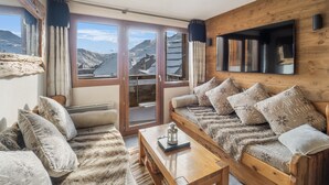 Une pièce chaleureuse avec un canapé en bois, une table en bois et une grande fenêtre donnant sur une vue imprenable sur les montagnes.