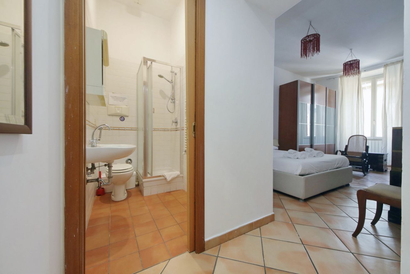 A hotel room with a bathroom, a bed, a chair, and a window.