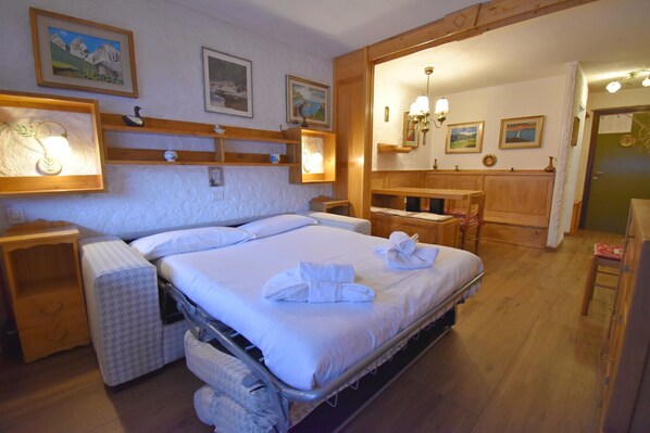 A hotel room with a large bed, wooden headboard, bedside tables, a mirror, and artwork on the walls. - NARDIS 109 APPARTAMENTO (Madonna di Campiglio)
