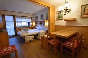 A cozy room with a bed, a table, and chairs. There are wall-mounted shelves with decorative items and a chandelier. - NARDIS 109 APPARTAMENTO (Madonna di Campiglio)