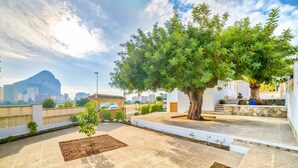 A rooftop garden with a large tree, stone tiles, and a view of a cityscape including a mountain. - Villa Garrofer- PlusHolidays (Calpe)