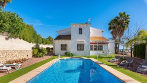 A swimming pool with a tiled deck, a white building with a red-tiled roof, and a stone wall. - Villa Padilla - PlusHolidays (Benissa)