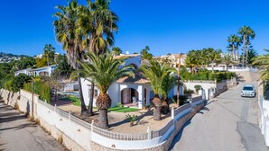 A white villa with a tiled roof, surrounded by palm trees and a stone wall. - Villa Padilla - PlusHolidays (Benissa)
