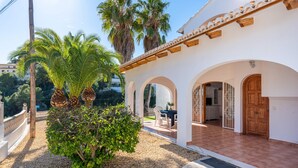 A white building with a tiled patio, palm trees, and a small garden area. - Villa Padilla - PlusHolidays (Benissa)