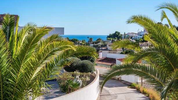 A coastal residential area with a curved road, palm trees, and houses with red-tiled roofs. - Villa Padilla - PlusHolidays (Benissa)