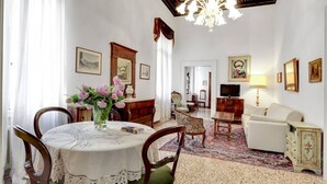 Ein Zimmer mit Esstisch, Stühlen, einer Couch, einem Fernseher und gerahmten Bildern an den Wänden.