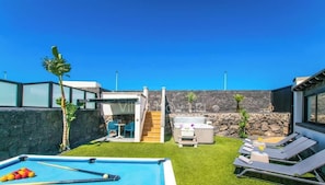 Un área de piscina con hidromasaje, sillones de descanso y una pared de piedra.