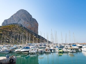 A marina with numerous sailboats docked, a prominent rocky cliff in the background, and a clear blue sky. - Villa Neus - PlusHolidays (Calpe)