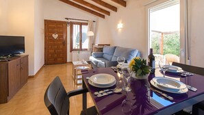 Un coin repas avec un plafond en bois, un canapé, un téléviseur et une table dressée pour deux personnes, avec des assiettes, des verres et des couverts.