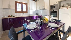 Une cuisine moderne avec des meubles de couleur violette, une table à manger dressée avec des assiettes et des verres à vin, et une enseigne indiquant « LE CAFÉ ».