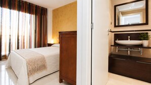 Habitación de hotel con cama, cómoda de madera, baño con lavabo y espejo, y ventana con cortinas.