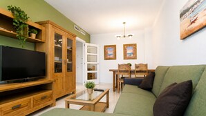 Una sala de estar con un sofá verde, armarios de madera, un televisor y un comedor con una mesa y sillas.