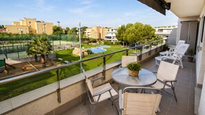 Un balcón con mesa y sillas, una piscina pequeña y vistas a edificios y follaje.