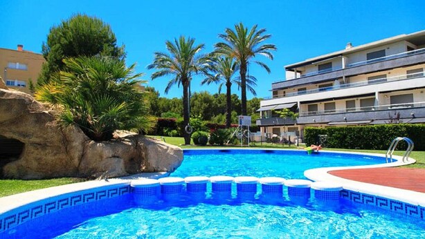 Una piscina con borde de mosaico azul, rodeada de palmeras y una gran roca.