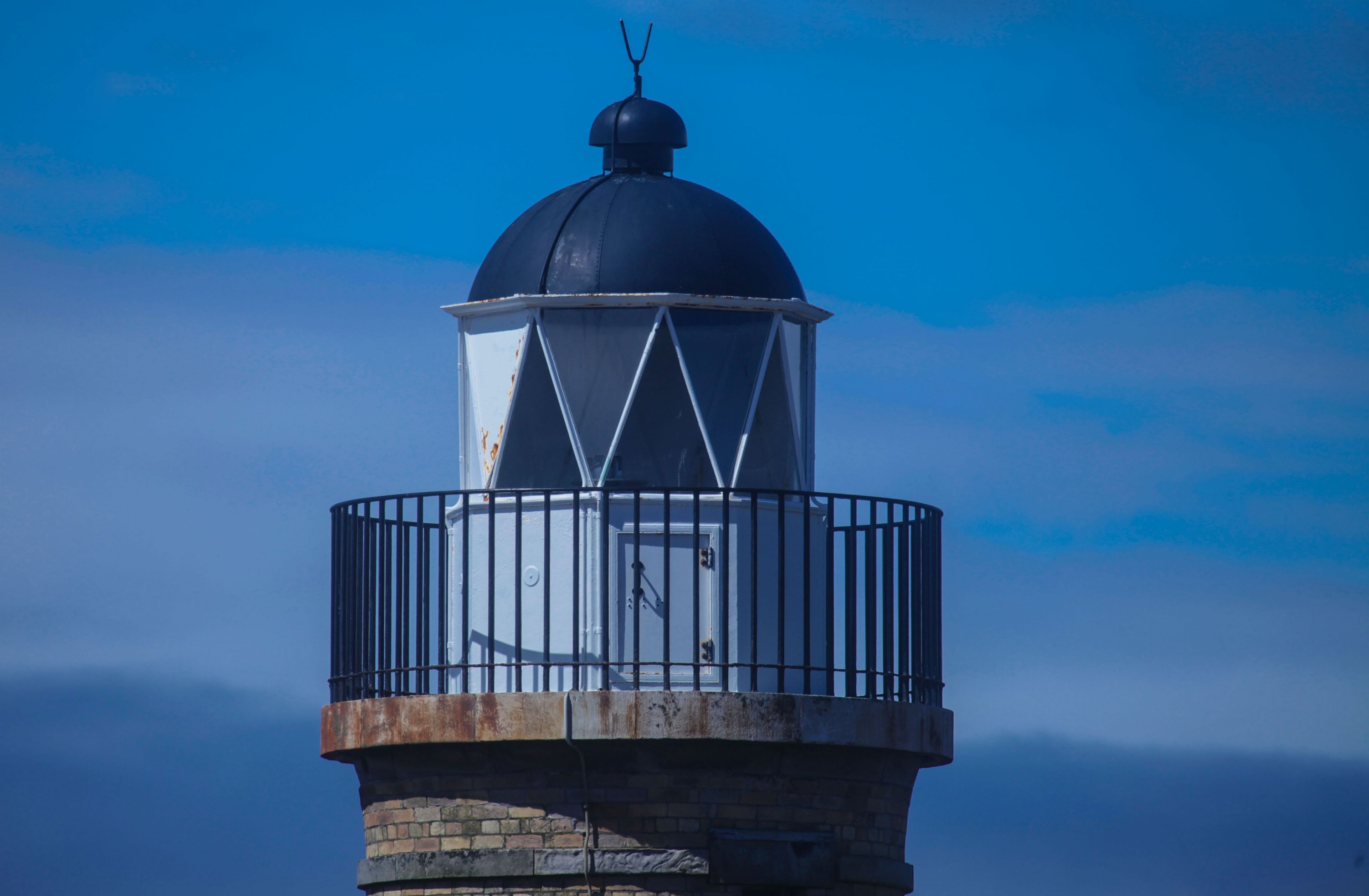 A lighthouse with a metal railing and a door, set against a clear sky.