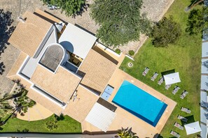 An aerial view of a modern house with a swimming pool, a covered patio, and a well-maintained lawn. - Peaceful villa with heatable pool in Almancil (Faro)