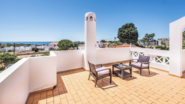 Eine Terrasse mit Meerblick, ausgestattet mit Korbstühlen und einem Tisch, sowie einer weißen Säulenstruktur.