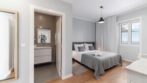 Quarto moderno com cama, mesa de cabeceira e vista para o mar pela janela.
