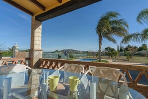 A glass table with chairs and a yellow mug, overlooking a pool and palm trees.