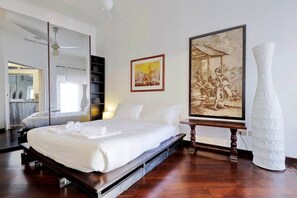 A modern bedroom with a large bed, a mirror, a painting, and a white vase.