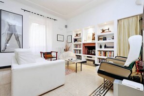 A modern living room with a white sofa, a reading chair, a bookshelf, and a fireplace.