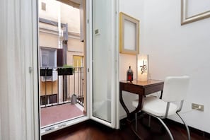 A room with a sliding glass door leading to a balcony, a small table with a chair, and a wall-mounted light fixture.