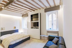 A bedroom with a bed, a built-in TV shelf, a window, and a sofa.