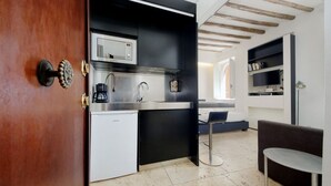 Cocina compacta con microondas integrado, cafetera y un refrigerador pequeño. Hay un comedor con una mesa y un banco.