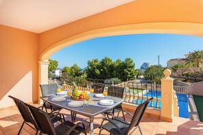 Comedor con mesa para dos, con vista a una piscina, árboles y edificios.