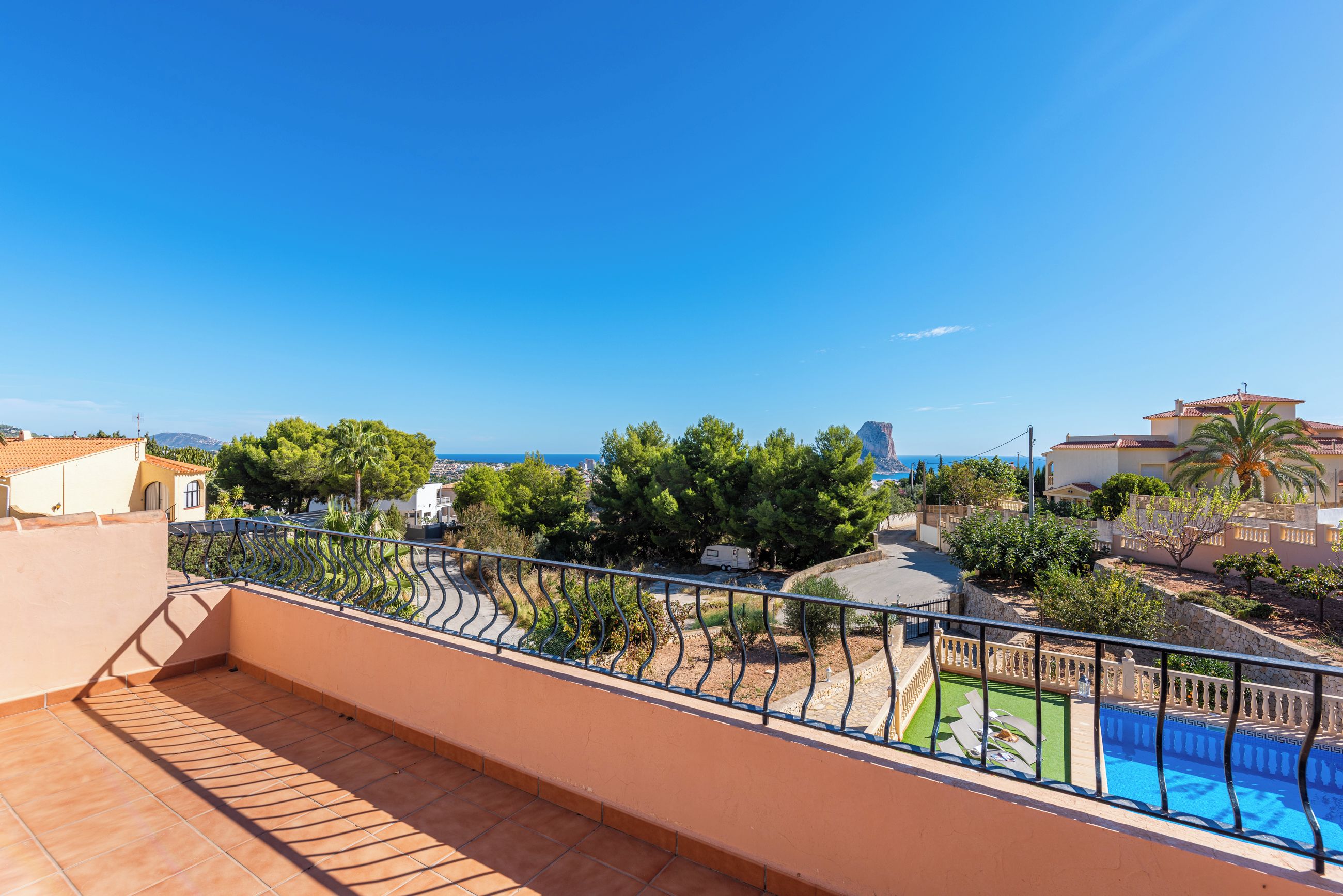 A rooftop terrace with a swimming pool, a view of the sea, and surrounding greenery.