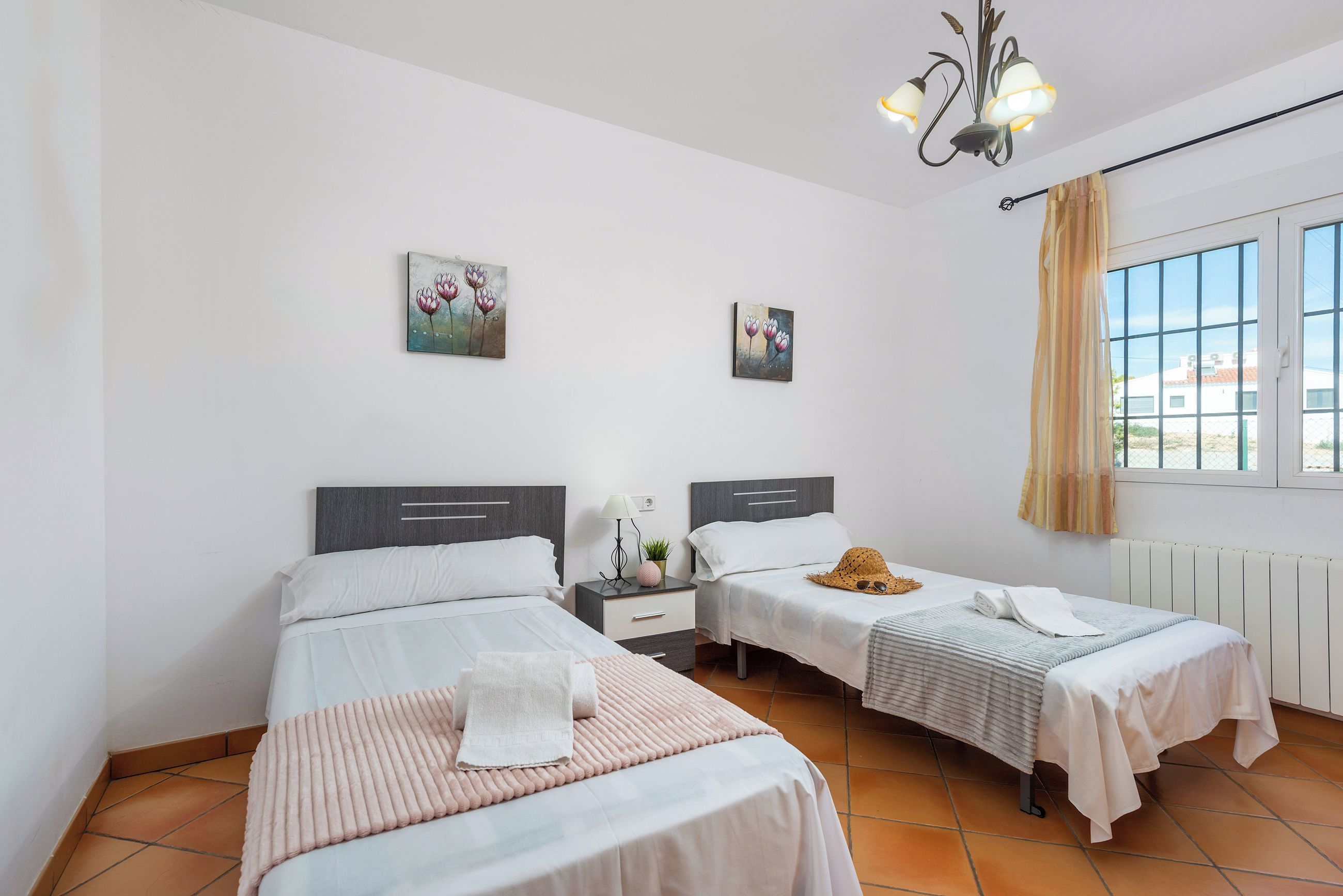 A hotel room with two beds, a nightstand with a lamp, a painting on the wall, and a window with curtains.