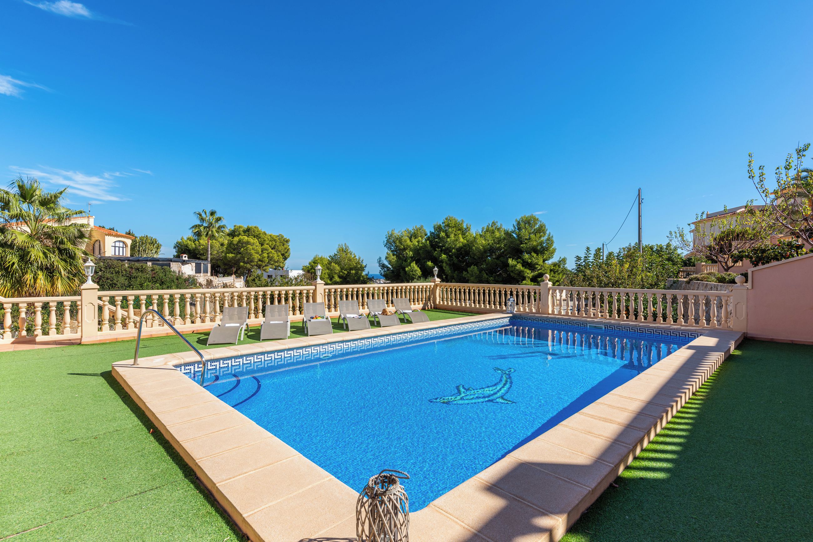 A rectangular swimming pool with a clear blue water surface, surrounded by a low white fence and a green lawn.