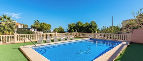 A rectangular swimming pool with a clear blue water surface, surrounded by a low white fence and a green lawn.