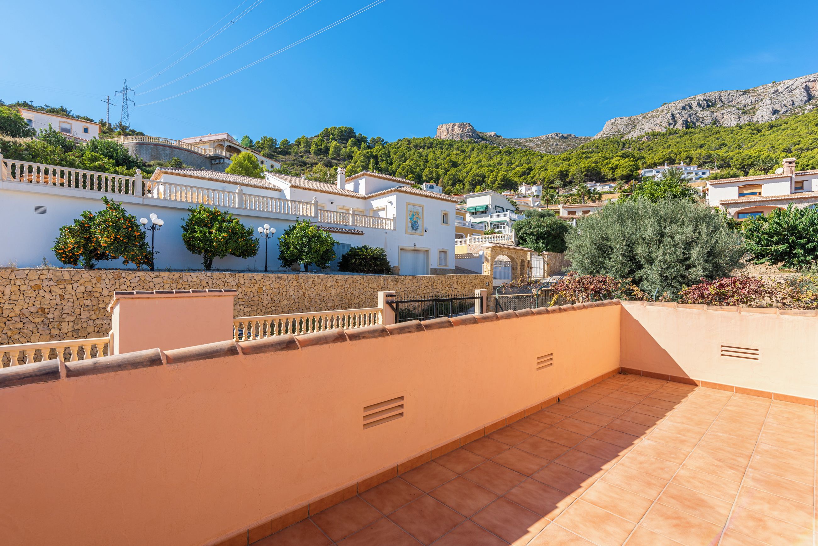 Zona residencial con tejados de tejas de color terracota, edificios blancos con balcones y montañas al fondo.