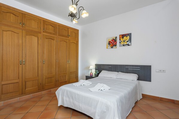 Un dormitorio con un armario amplio, una cama con ropa de cama blanca, dos obras de arte en la pared y un cabecero moderno.
