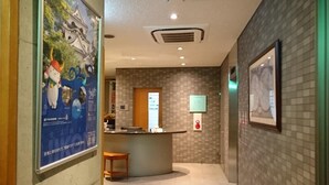 Eine Hotelhalle mit einer Rezeption, einer kleinen Sitzecke und einer gefliesten Wand.