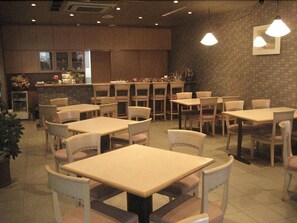 A restaurant with multiple tables and chairs, a counter with a display case, and a brick wall.