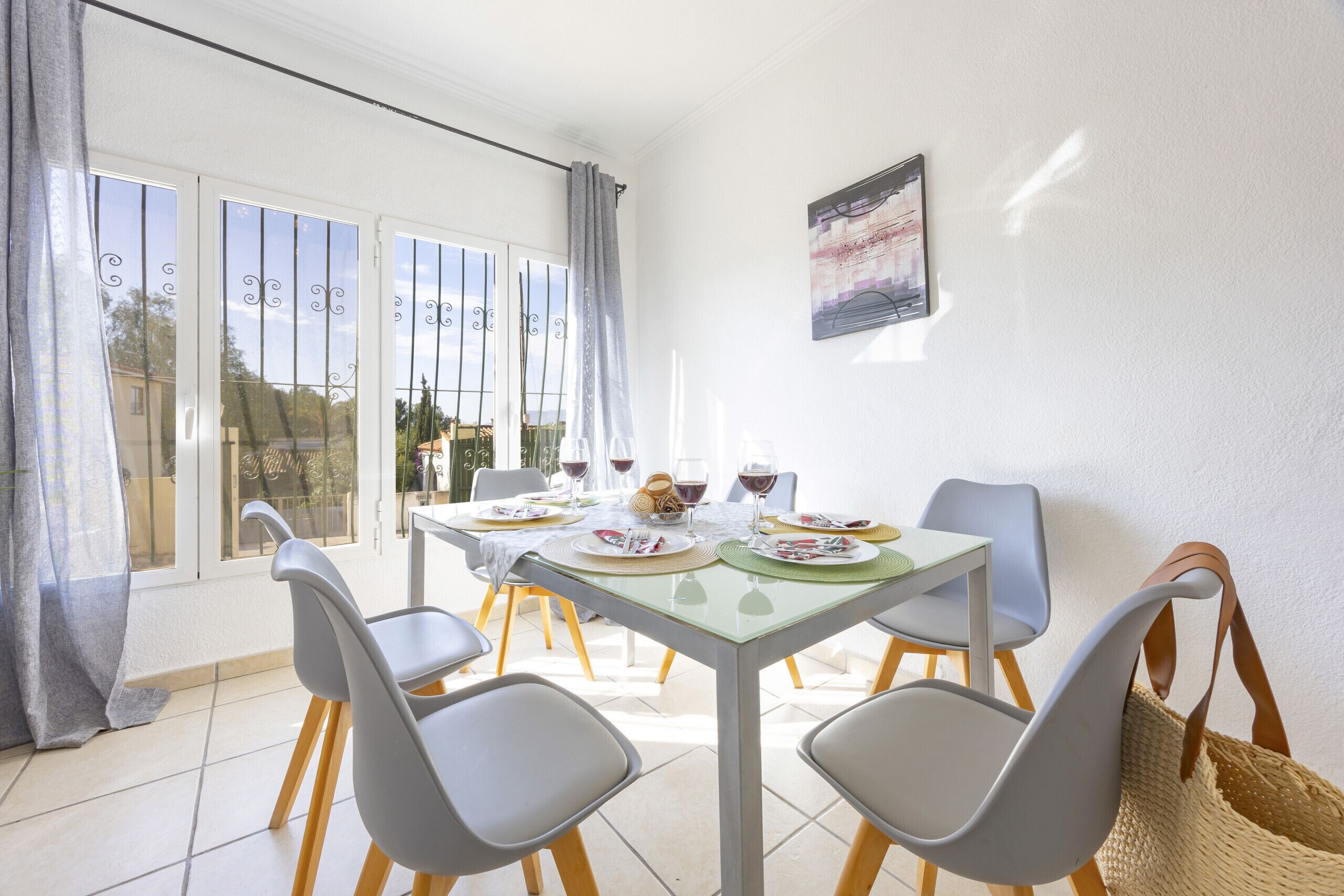 Un coin repas avec une table dressée pour quatre personnes, des chaises, une fenêtre avec des rideaux et une vue sur l’extérieur.