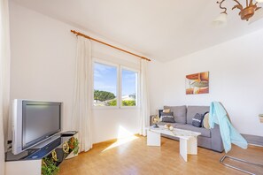 A modern living room with a flat-screen TV, a sofa, a coffee table, and a window with curtains.