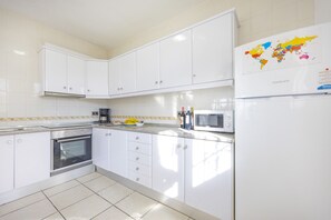 A kitchen with white cabinets, a stove, a microwave, and a world map on the refrigerator.