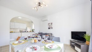 A modern dining area with a table set for a meal, a television, and a kitchen in the background. - Villa Carola - PlusHolidays (Calpe)