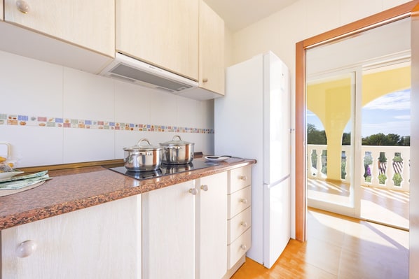 Una cocina con gabinetes blancos, encimera de granito y refrigerador blanco. Hay ollas en la estufa y una ventana con vista a un balcón.