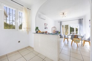 Una cocina amplia con una isla central, ventanas grandes y un comedor con sillas y una mesa.