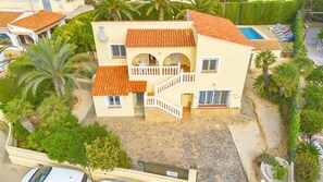 A two-story house with a tiled roof, a stone-paved courtyard, and a swimming pool.