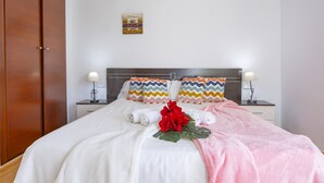 A neatly made bed with white linens, two pillows with zigzag patterns, a pink blanket, and a red flower centerpiece. - Villa Carola - PlusHolidays (Calpe)
