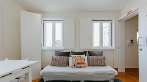 Ein kleiner, moderner Raum mit einem Bett, einem weißen Tisch und zwei Fenstern.