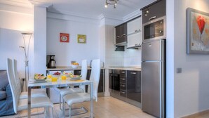 Une cuisine moderne équipée d’appareils électroménagers en acier inoxydable, un coin repas avec des chaises blanches et une petite table mise pour le petit-déjeuner.